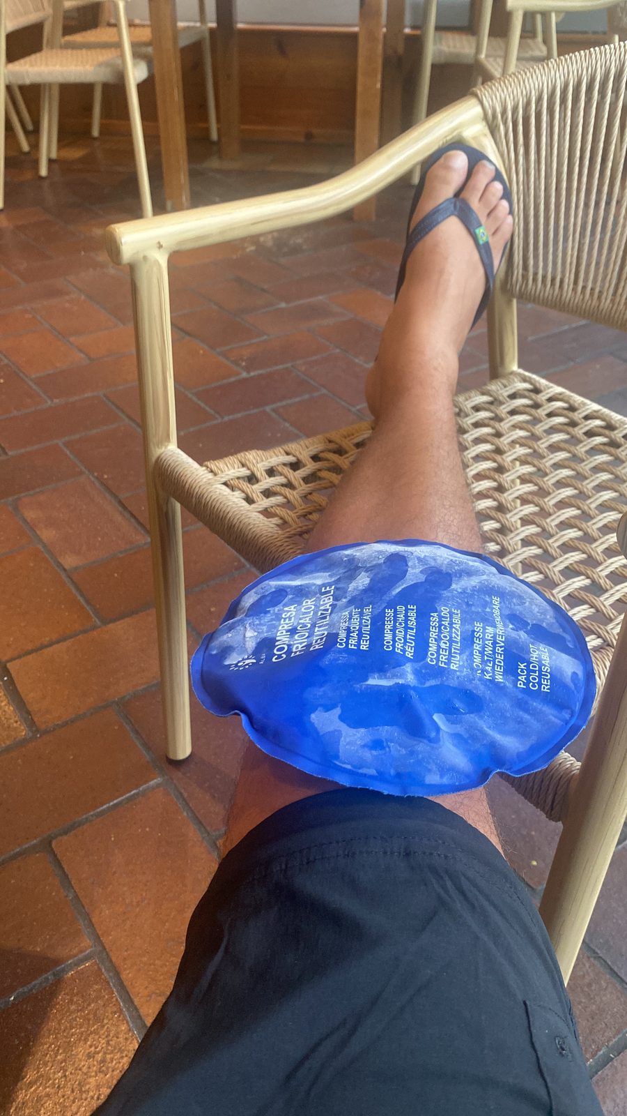 An ice pack resting on a knee propped up on a wicker cafe chair
