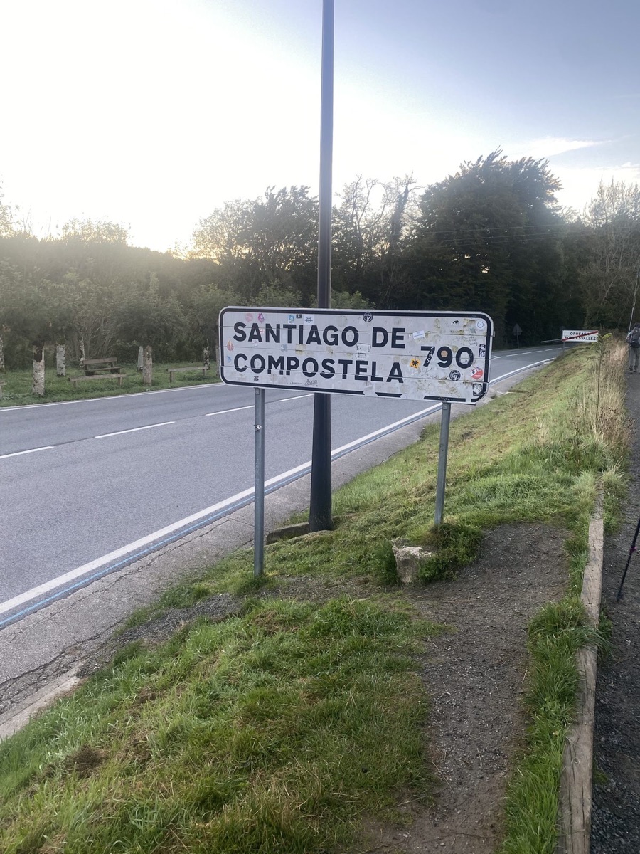 A road sign reading Santiago de Compostela 760 at the edge of a town