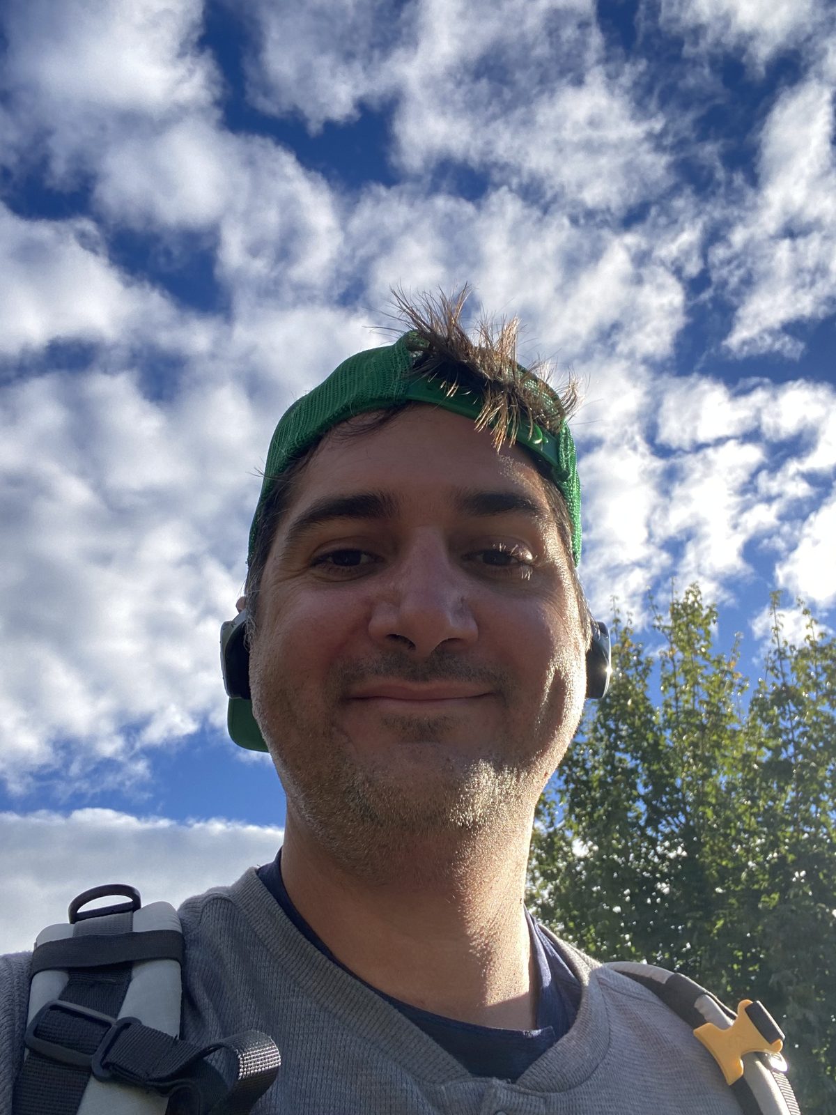 Smiling selfie in a green buff high in the mountains with clouds behind