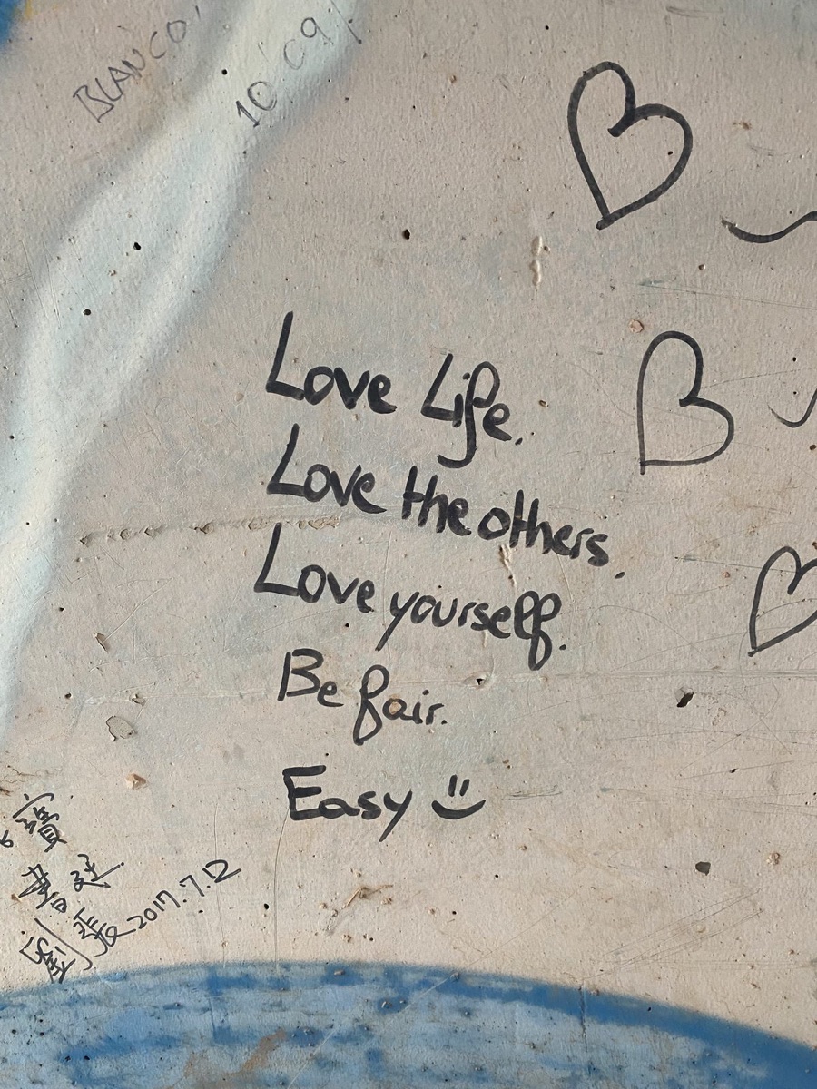 Handwriting on a wall reading Love Life, Love the others, Love yourself, Be fair, Easy with a smiley