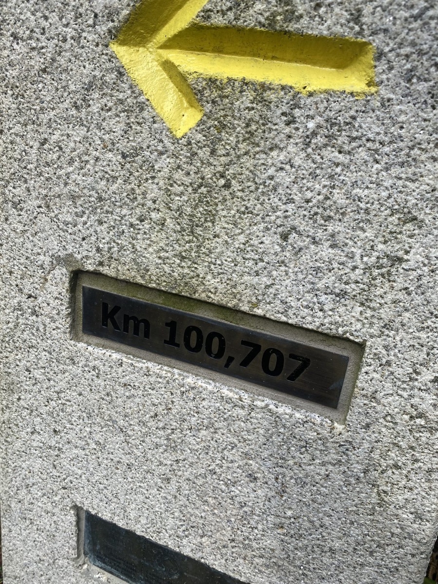 A stone Camino marker reading Km 100,707 with a yellow arrow