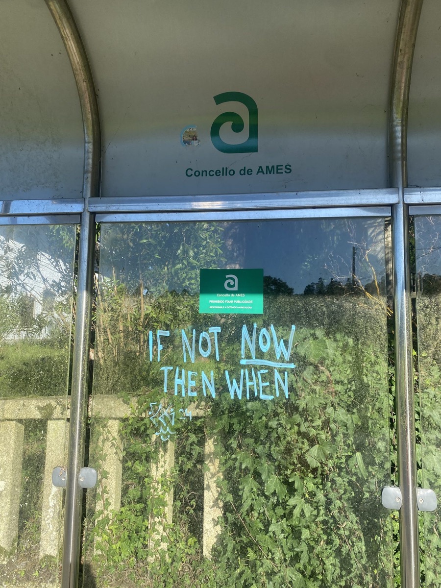 Words written on a glass bus shelter reading If not now then when